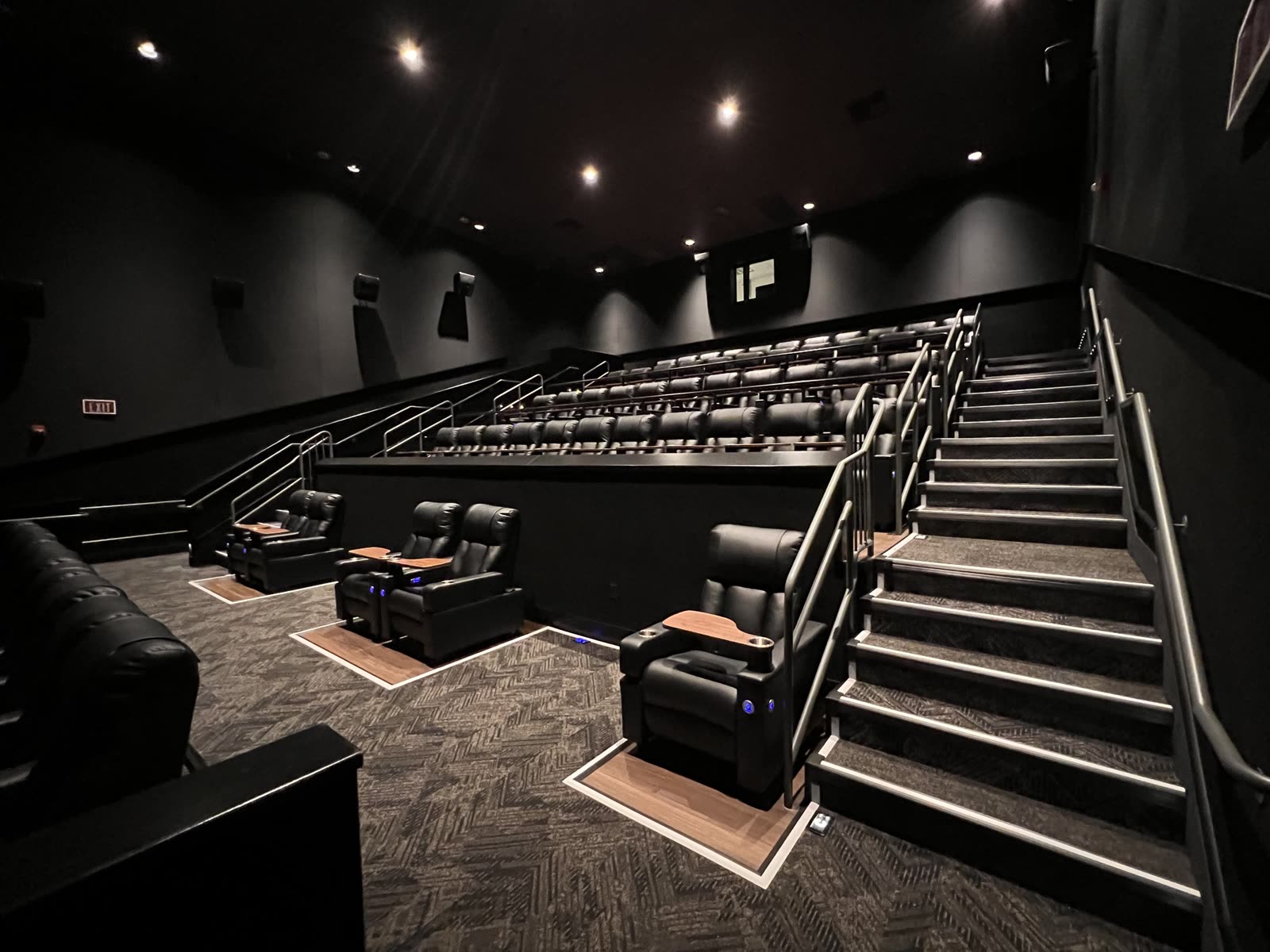 Completed cinema auditorium with tiered rows of black leather recliners, handrails and step lighting