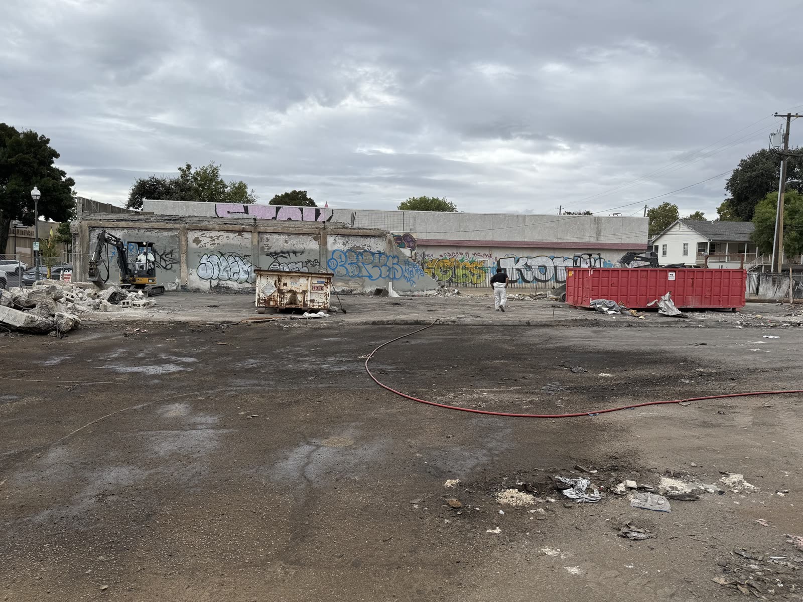 Commercial site part way through demolition with the tagged perimeter walls still up and roll-off bins staged on the slab