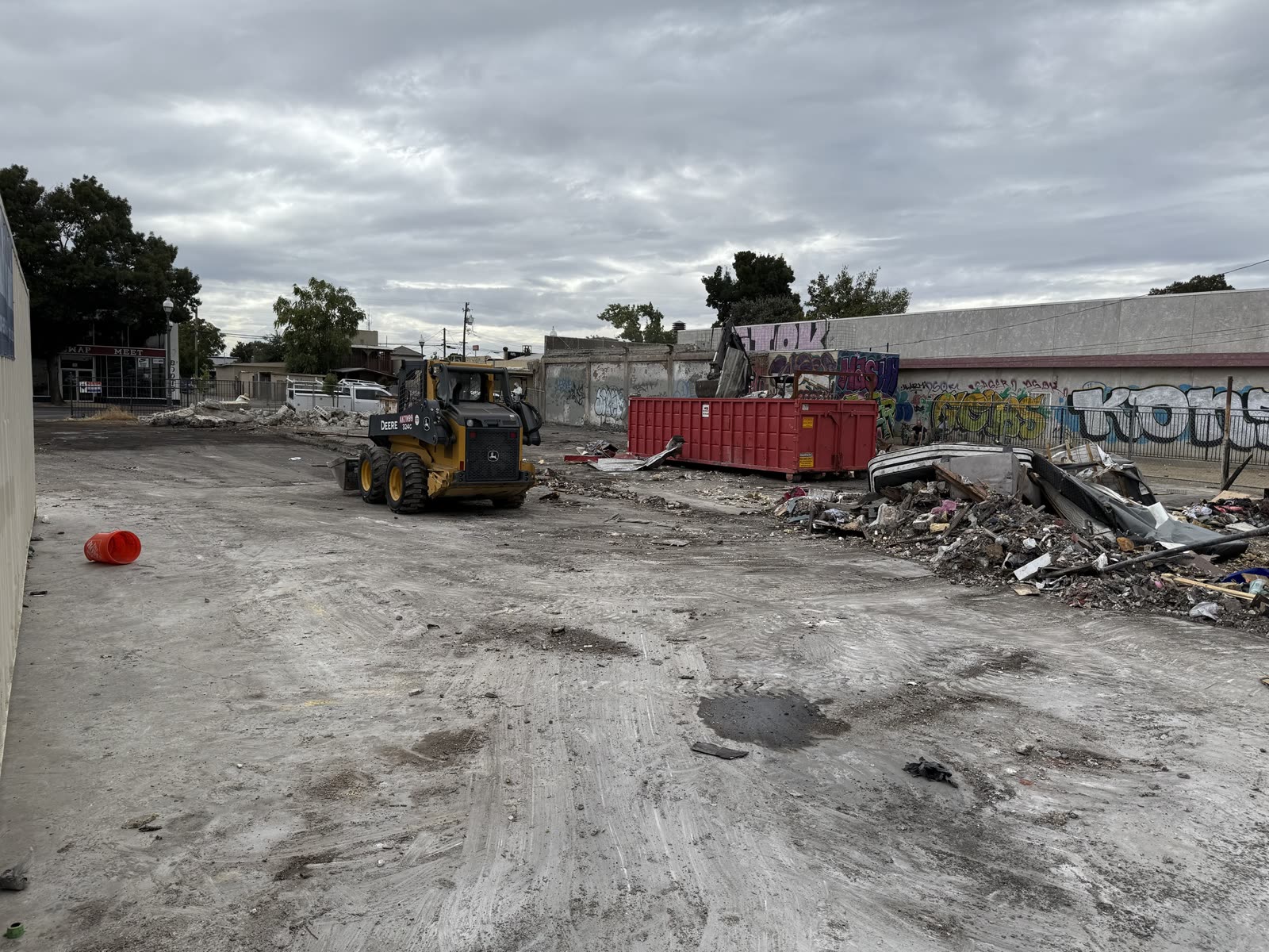Skid steer working the last of the demolition debris into a roll-off bin on a cleared commercial lot