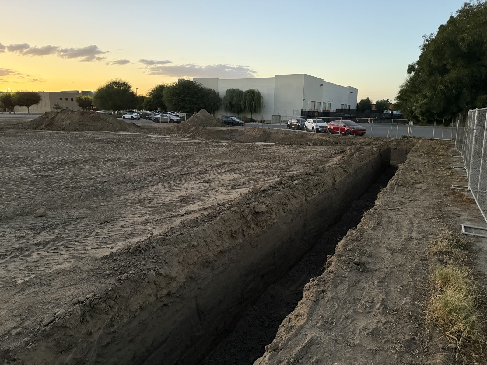 Long footing trench run out along the edge of a commercial pad at dusk with the building beyond