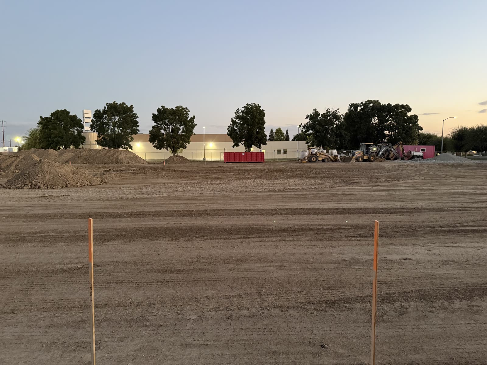 Graded commercial building pad at dusk with grade stakes set and the spoil heaps behind