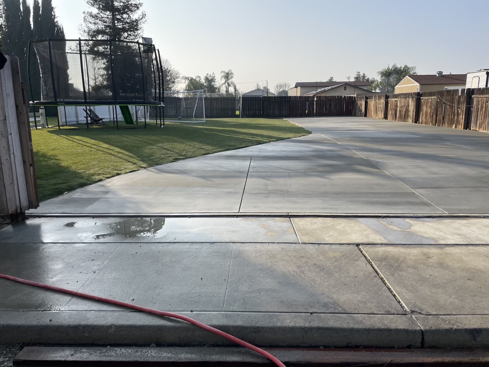 Cured concrete drive and slab washed down, curving around the turf lawn to the gate
