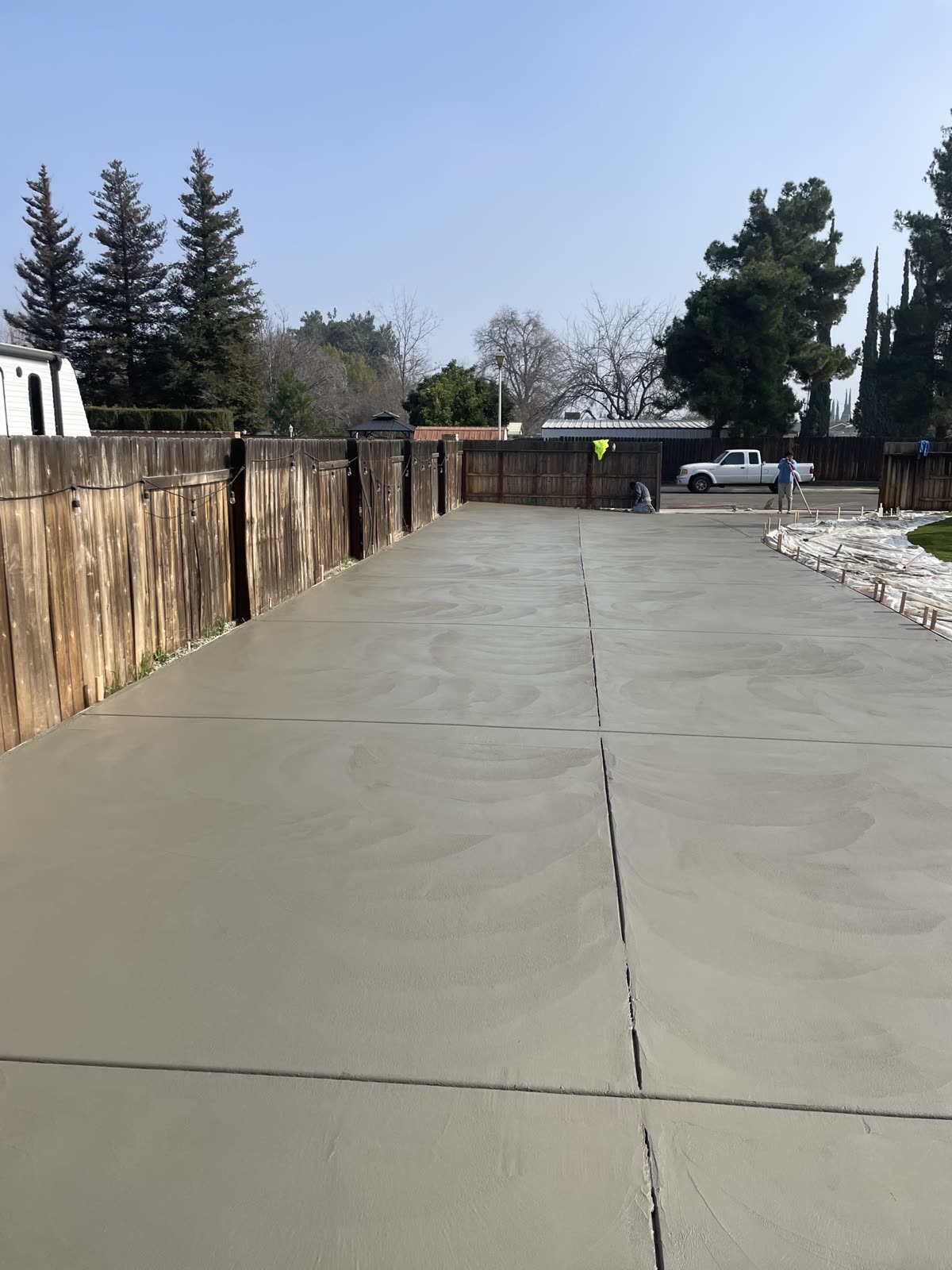 Long fresh concrete pour troweled smooth and jointed, running between the fence lines
