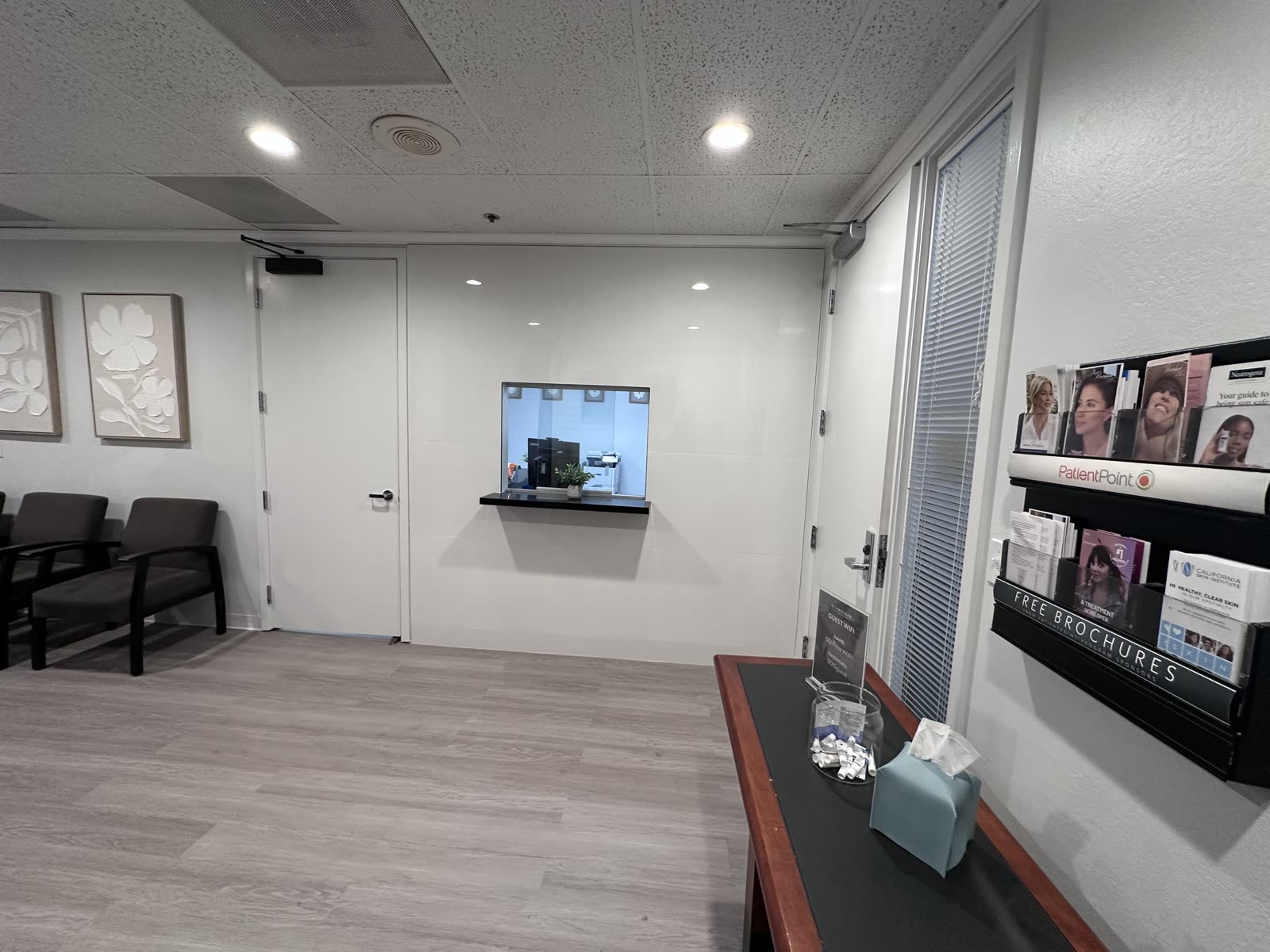 Finished reception transaction window with a stone sill, new doors and a wall-mounted brochure rack in a dermatology clinic