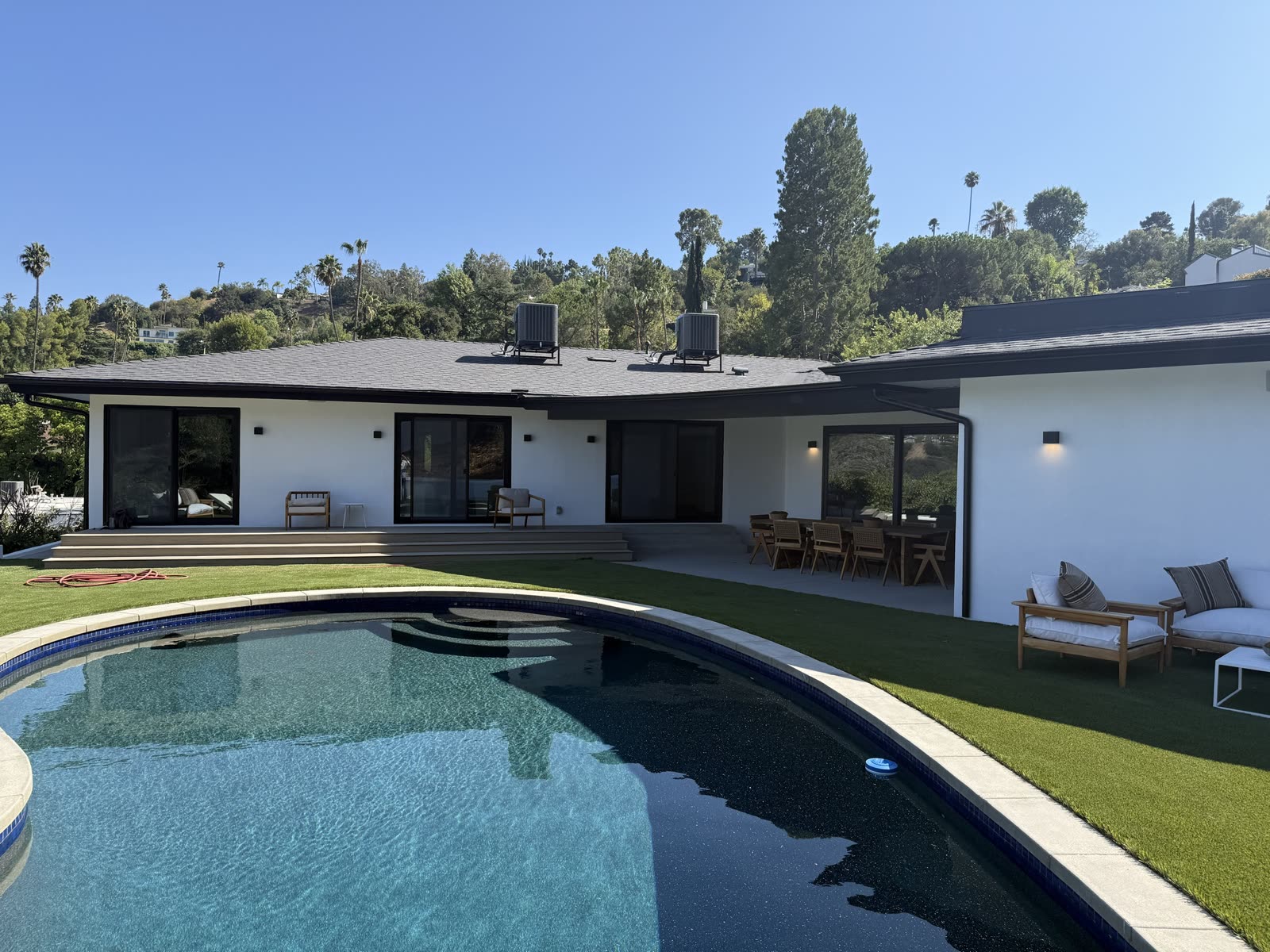 Wide view of the renovated rear elevation with new sliding glass doors, a raised deck, turf lawn and the swimming pool in the foreground