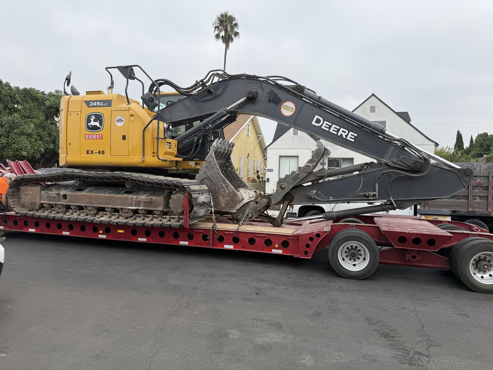 John Deere 245G LC excavator chained down on a lowboy trailer ready to leave a residential demolition site