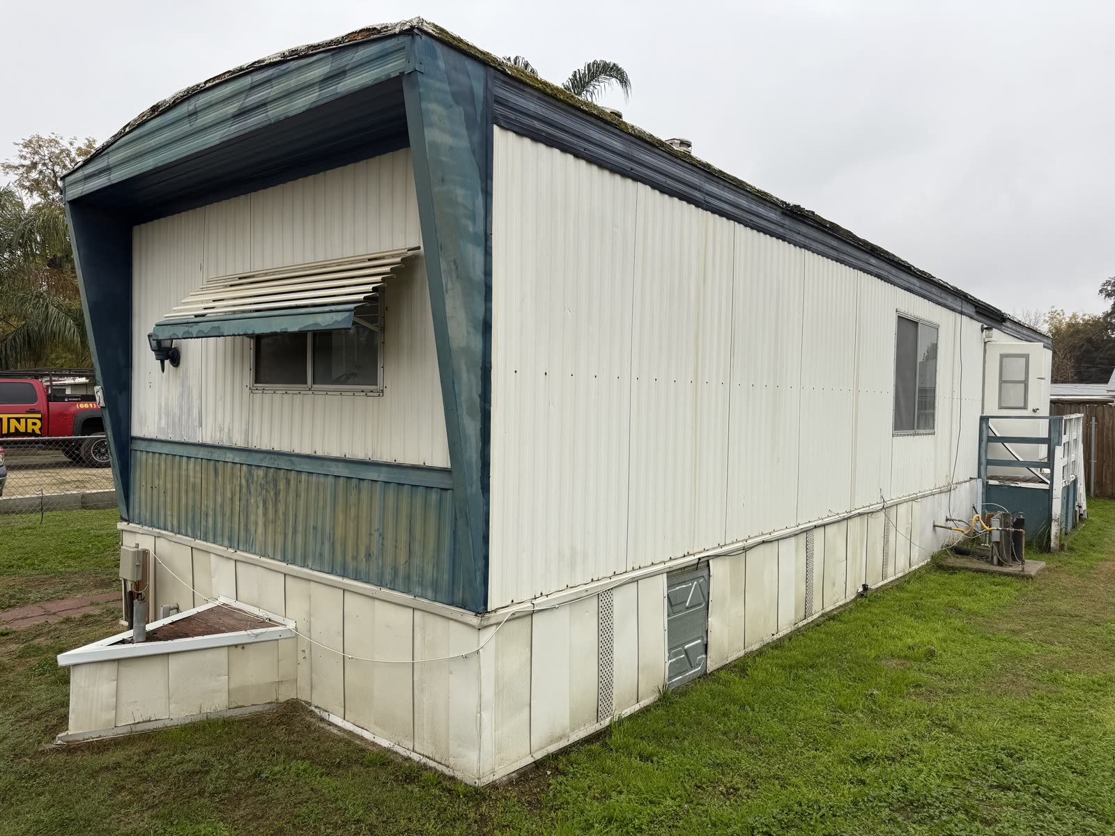 Side elevation of the same mobile home before removal, showing the skirting and window awnings