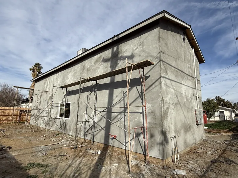 Scaffolding standing against a freshly brown-coated stucco wall part way through the render