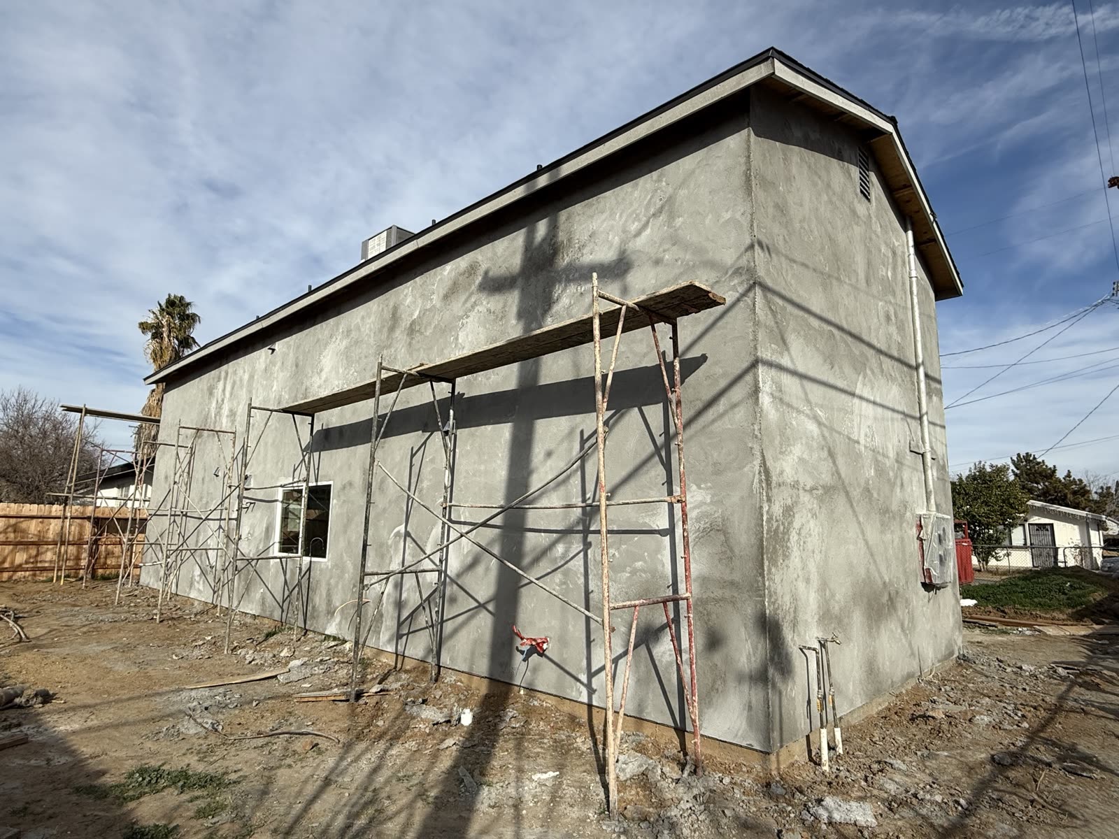 Scaffolding standing against a freshly brown-coated stucco wall part way through the render