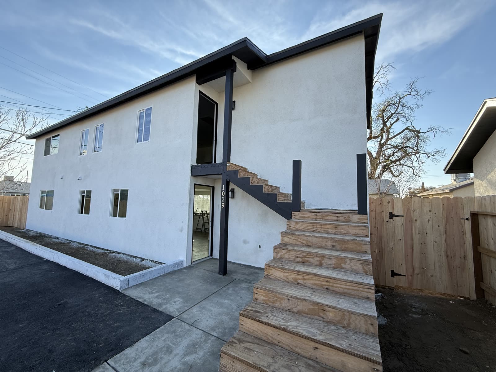 Finished white stucco apartment building with black trim, a new concrete walk and a timber entry stair