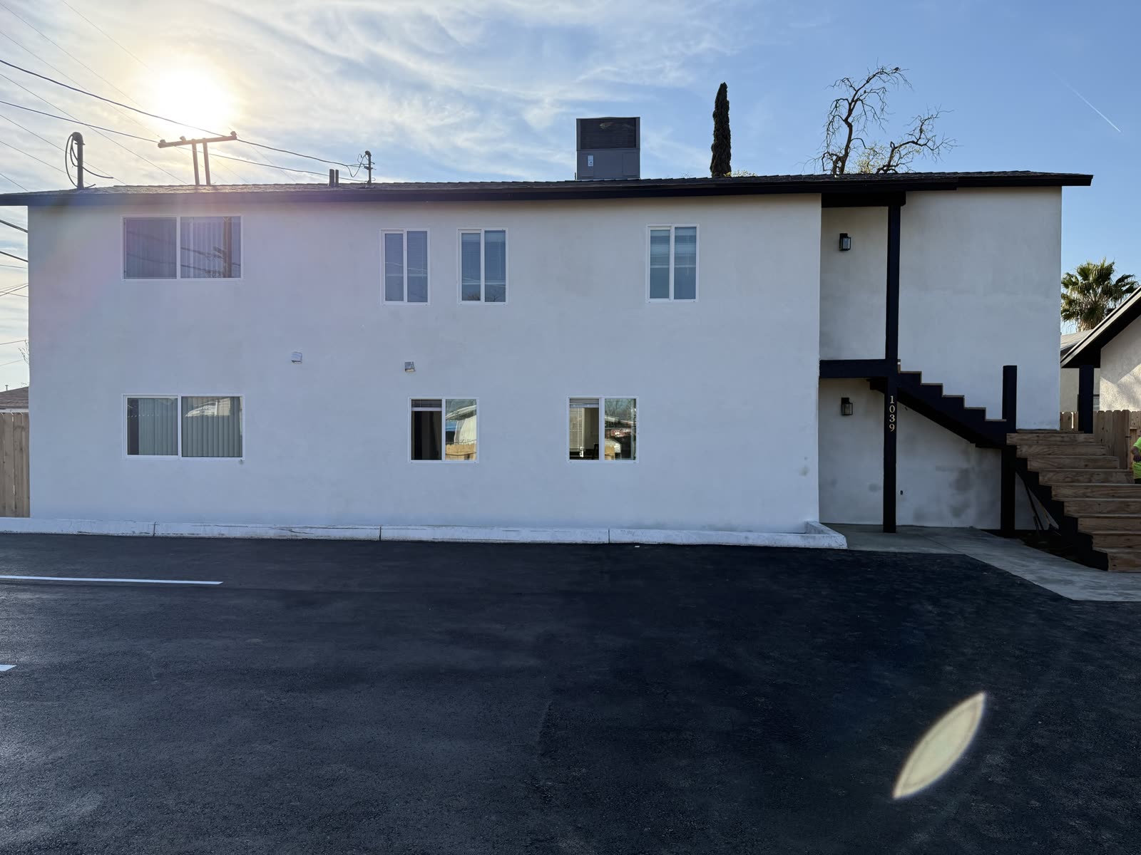 Finished apartment building in white stucco with black fascia, seen across the new asphalt parking lot