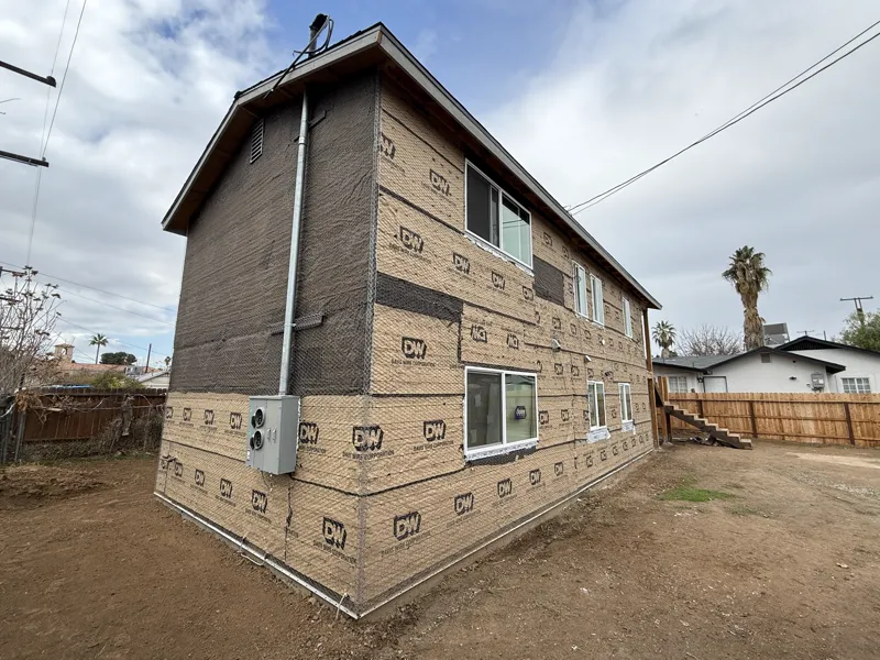 Two-story apartment building wrapped in building paper and wire lath, new vinyl windows set, ready for the scratch coat
