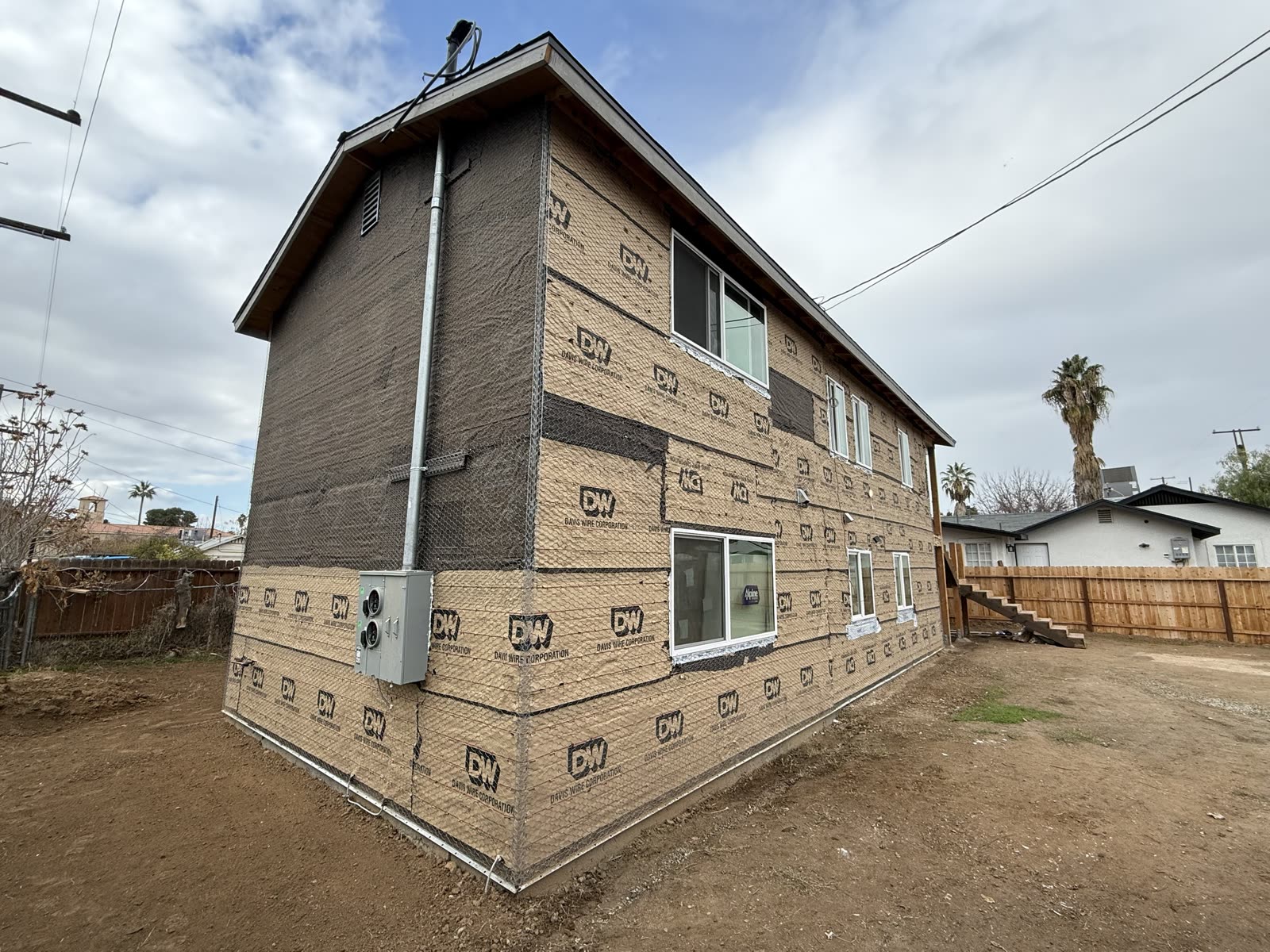 Two-story apartment building wrapped in building paper and wire lath, new vinyl windows set, ready for the scratch coat