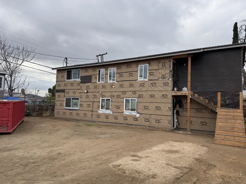 Rear elevation of an apartment building in lath and paper with new windows, a temporary stair and a roll-off bin