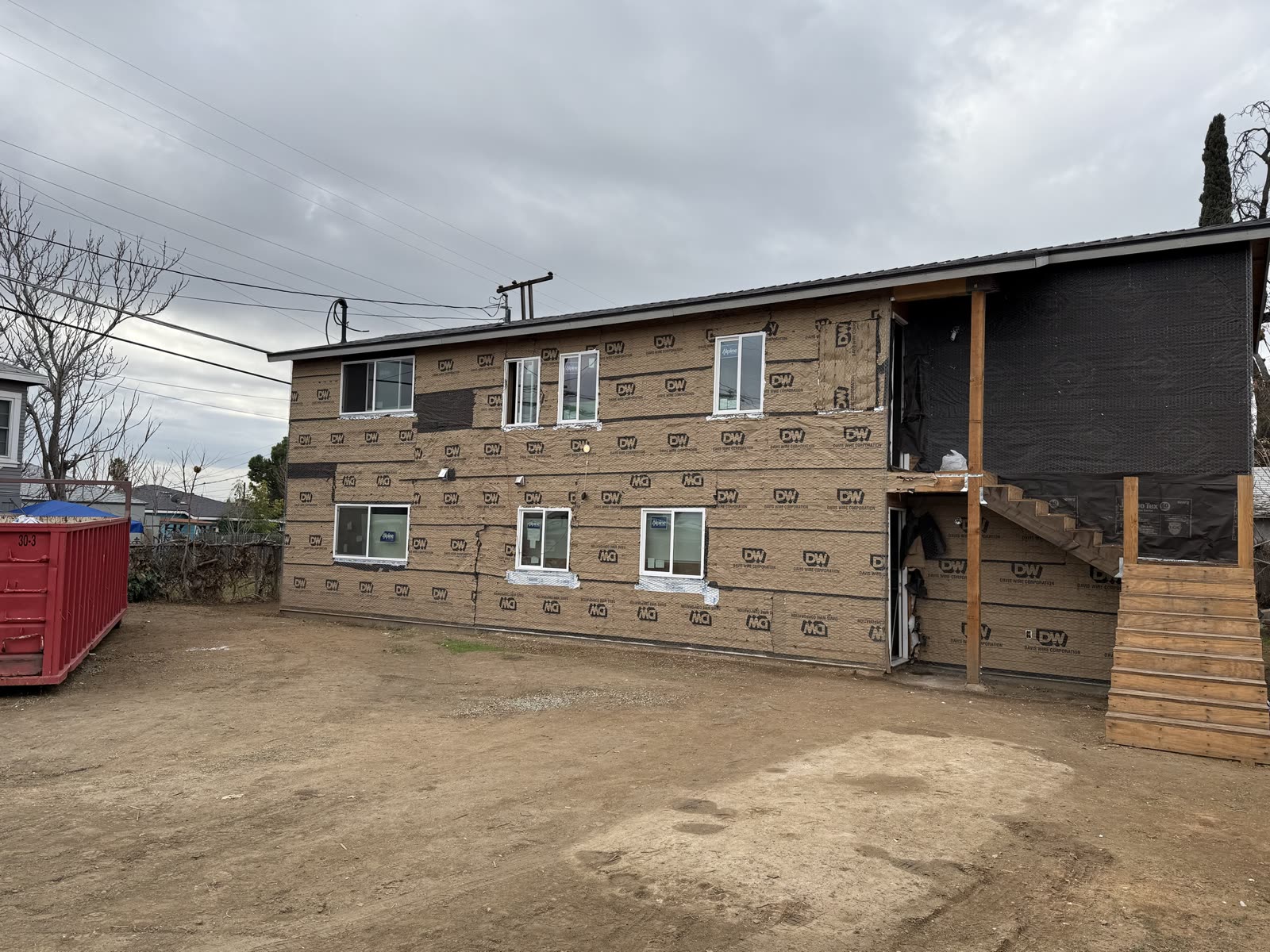Rear elevation of an apartment building in lath and paper with new windows, a temporary stair and a roll-off bin