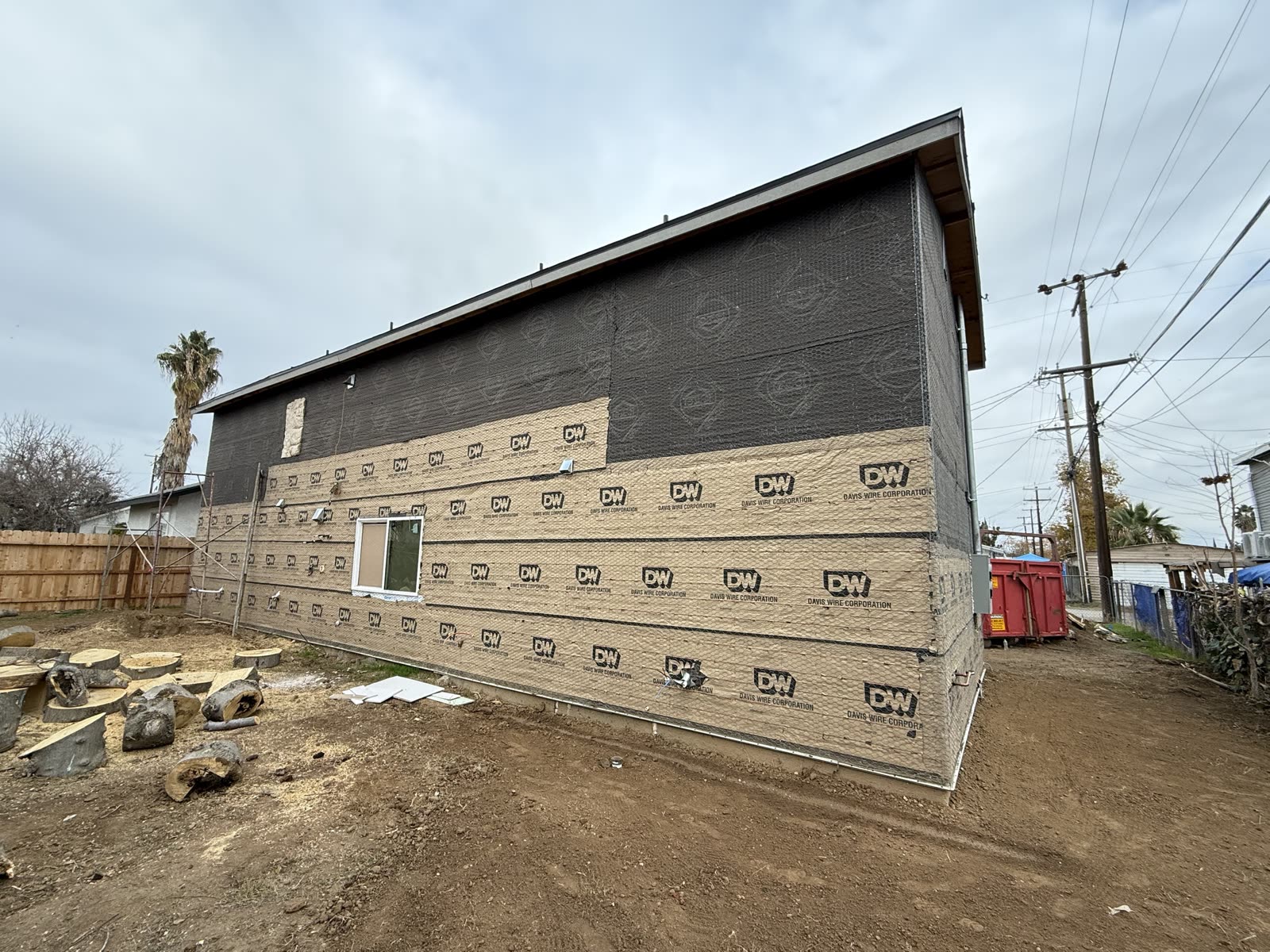 Long side elevation of an apartment building in wire lath and paper with a roll-off bin staged in the side yard