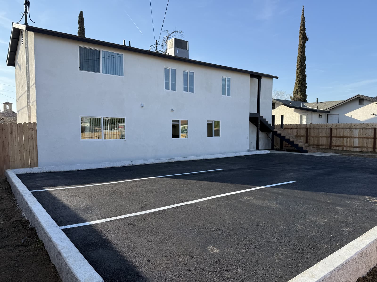 Newly paved and striped asphalt parking lot with fresh concrete curbing alongside the finished building
