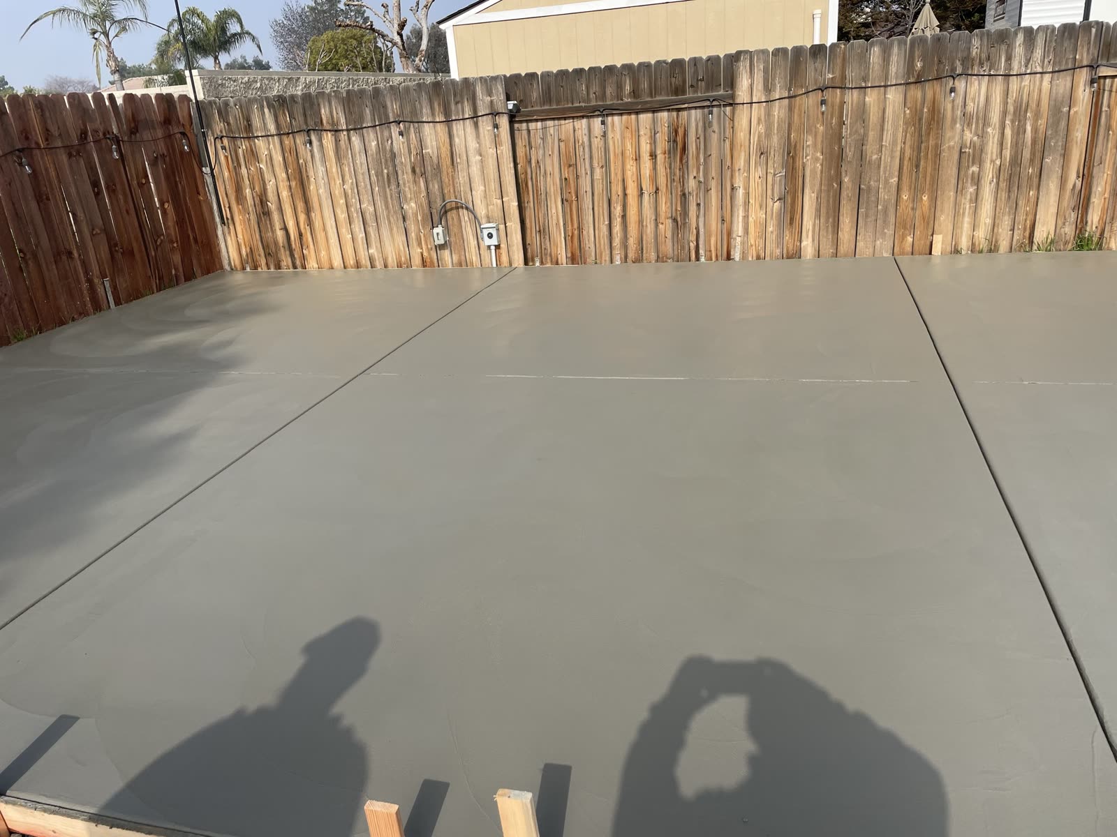 Finished residential concrete slab troweled smooth and jointed, running wall to wall behind the fence