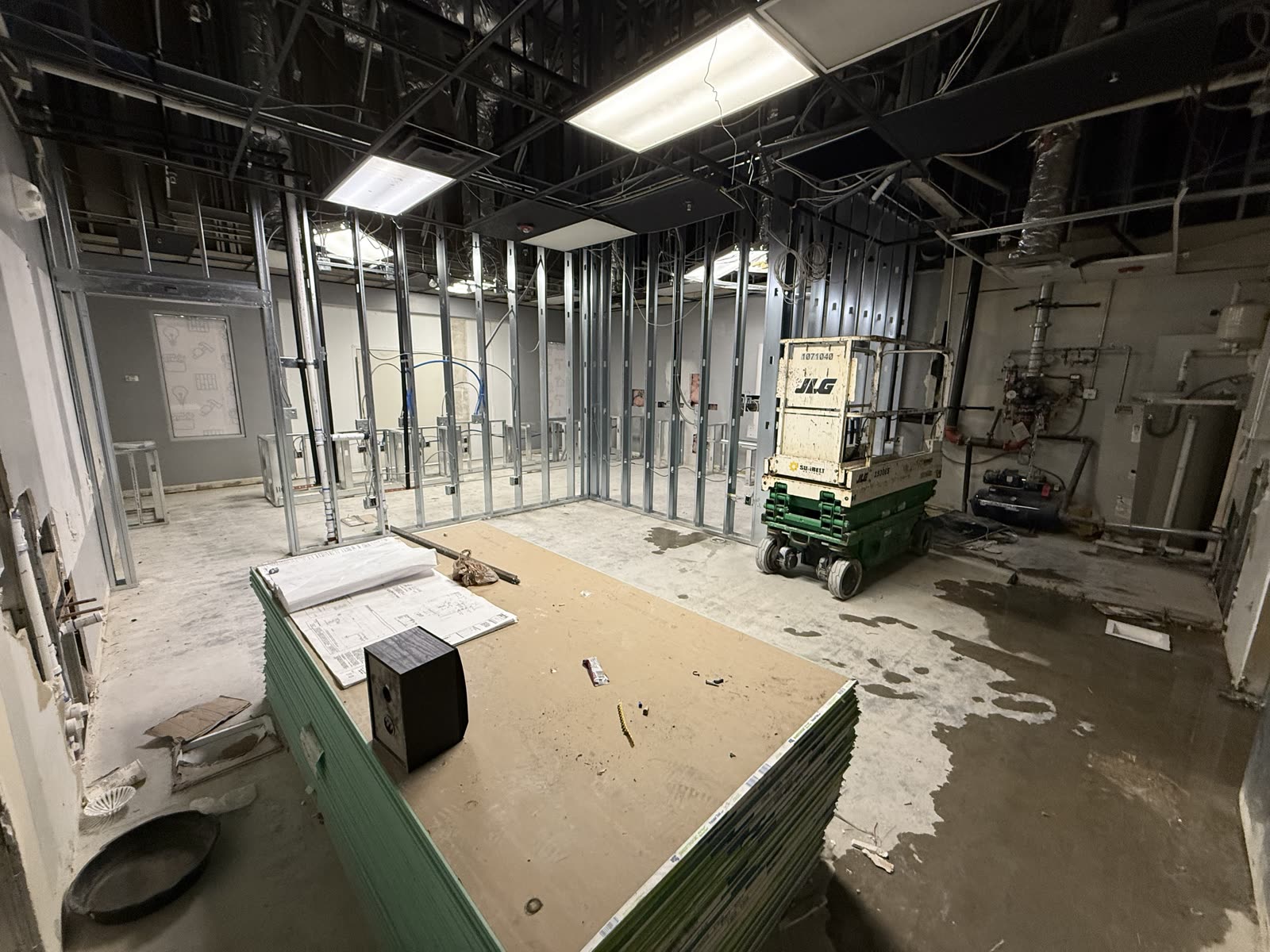 Scissor lift parked among metal stud partitions while overhead services are roughed in