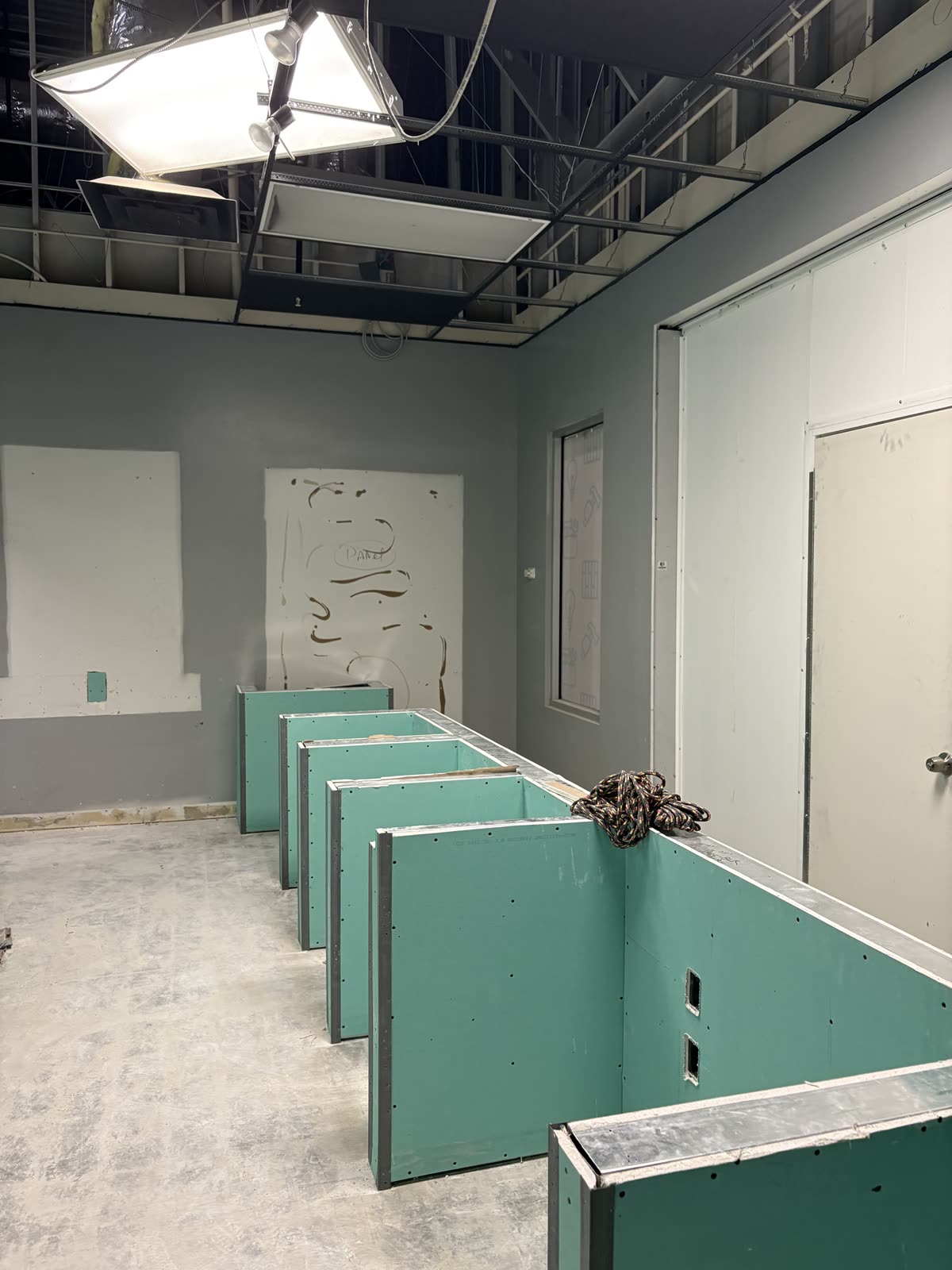 Run of newly boarded partitions in a commercial fit-out with the slab swept and lighting temporary