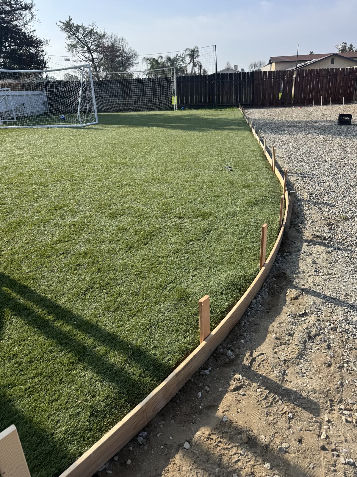 Timber form holding a clean edge between the artificial turf lawn and the new base rock