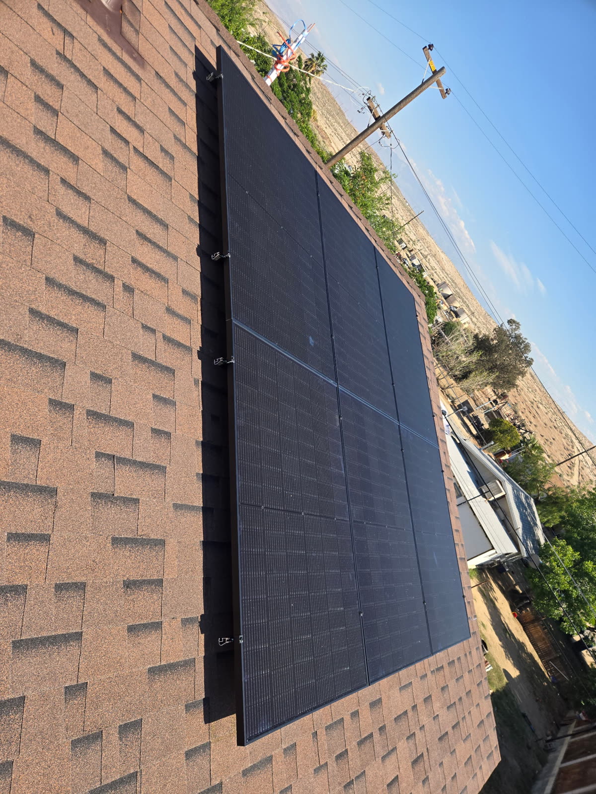 Black solar panels installed along the edge of a composition shingle roof against a clear sky