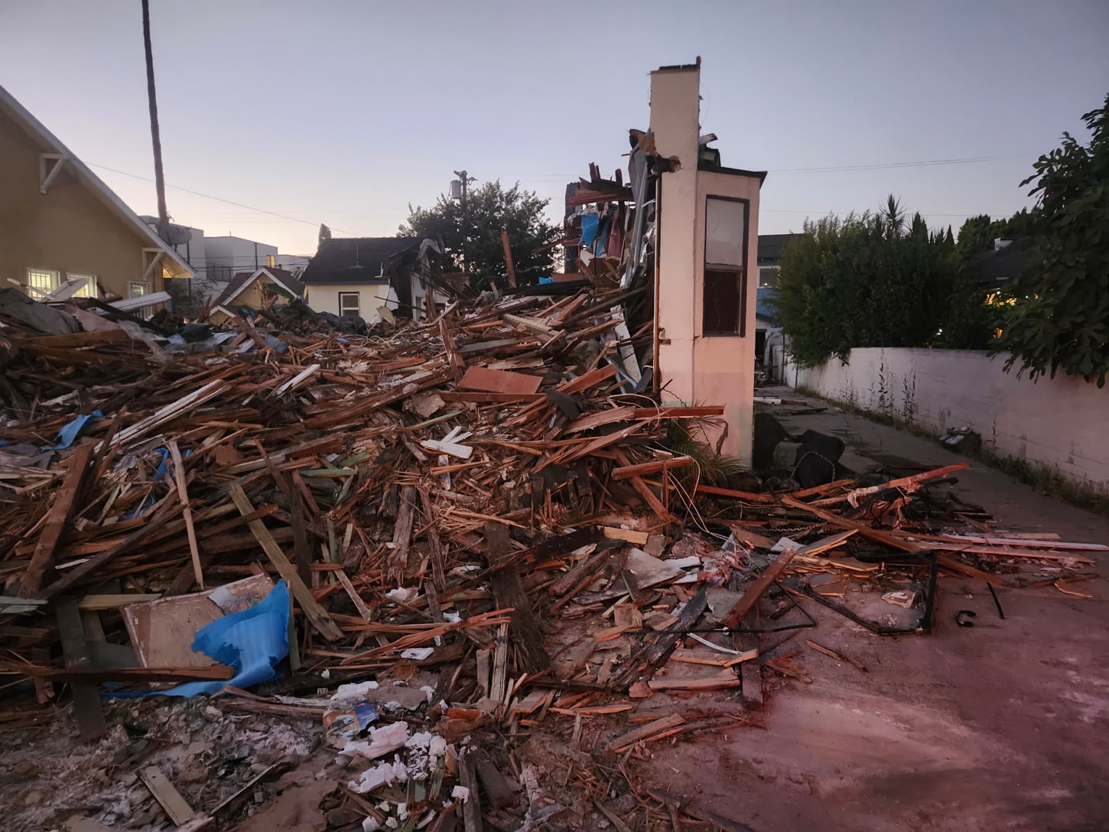 House taken down to a standing brick chimney with the framing and roof stacked as debris ready for haul-off
