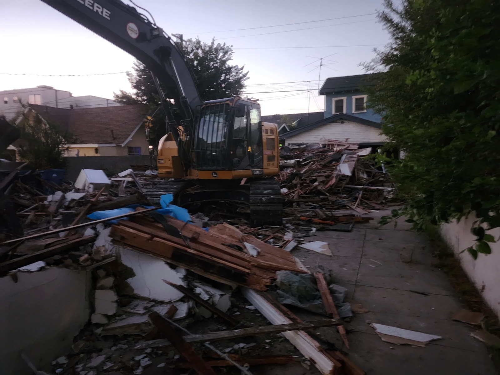 Tracked excavator standing on a demolished house working the debris pile down into the driveway at dusk