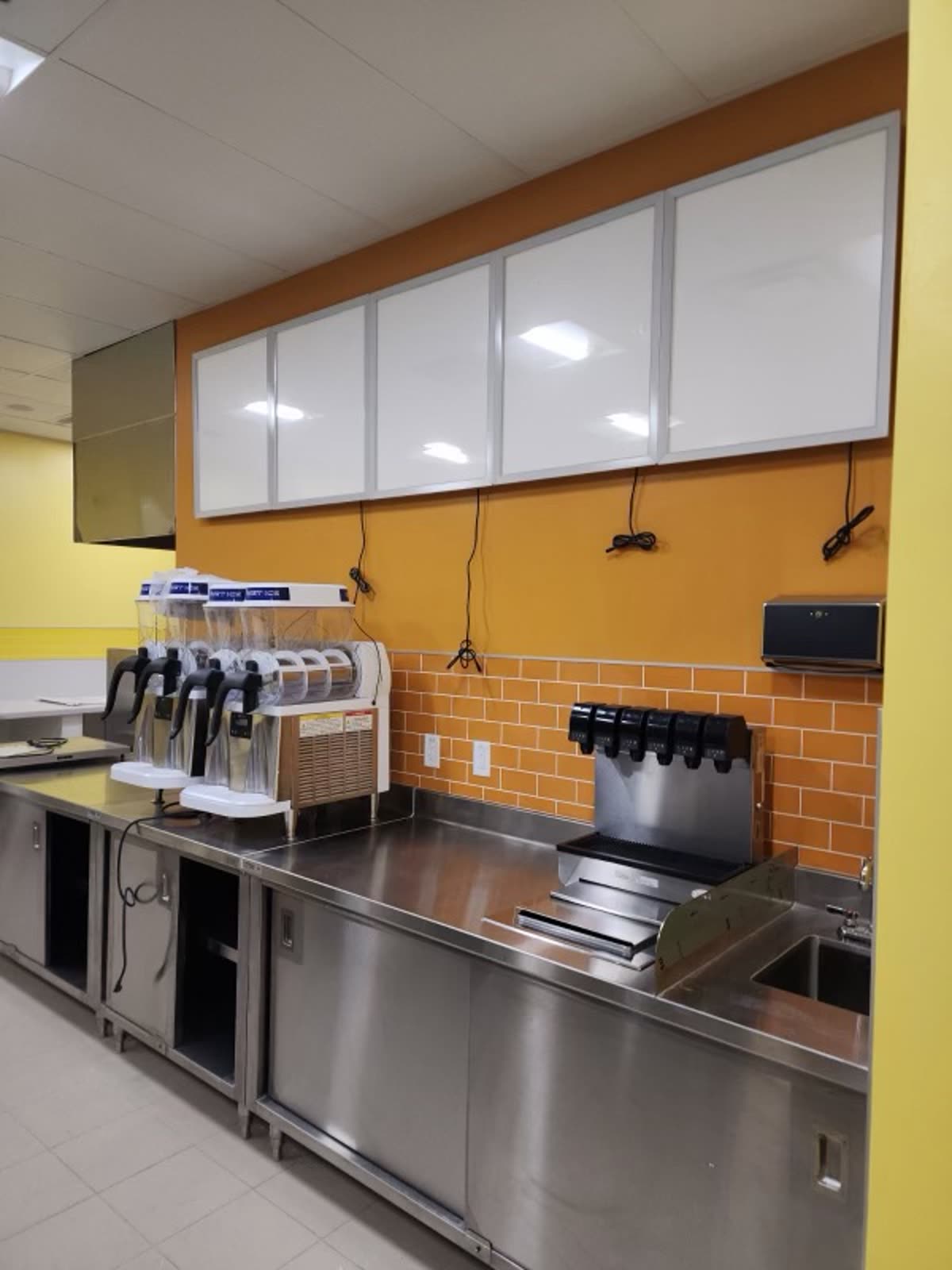 Completed beverage station with stainless counters, a frozen drink machine, soda tower and hand sink against orange tile
