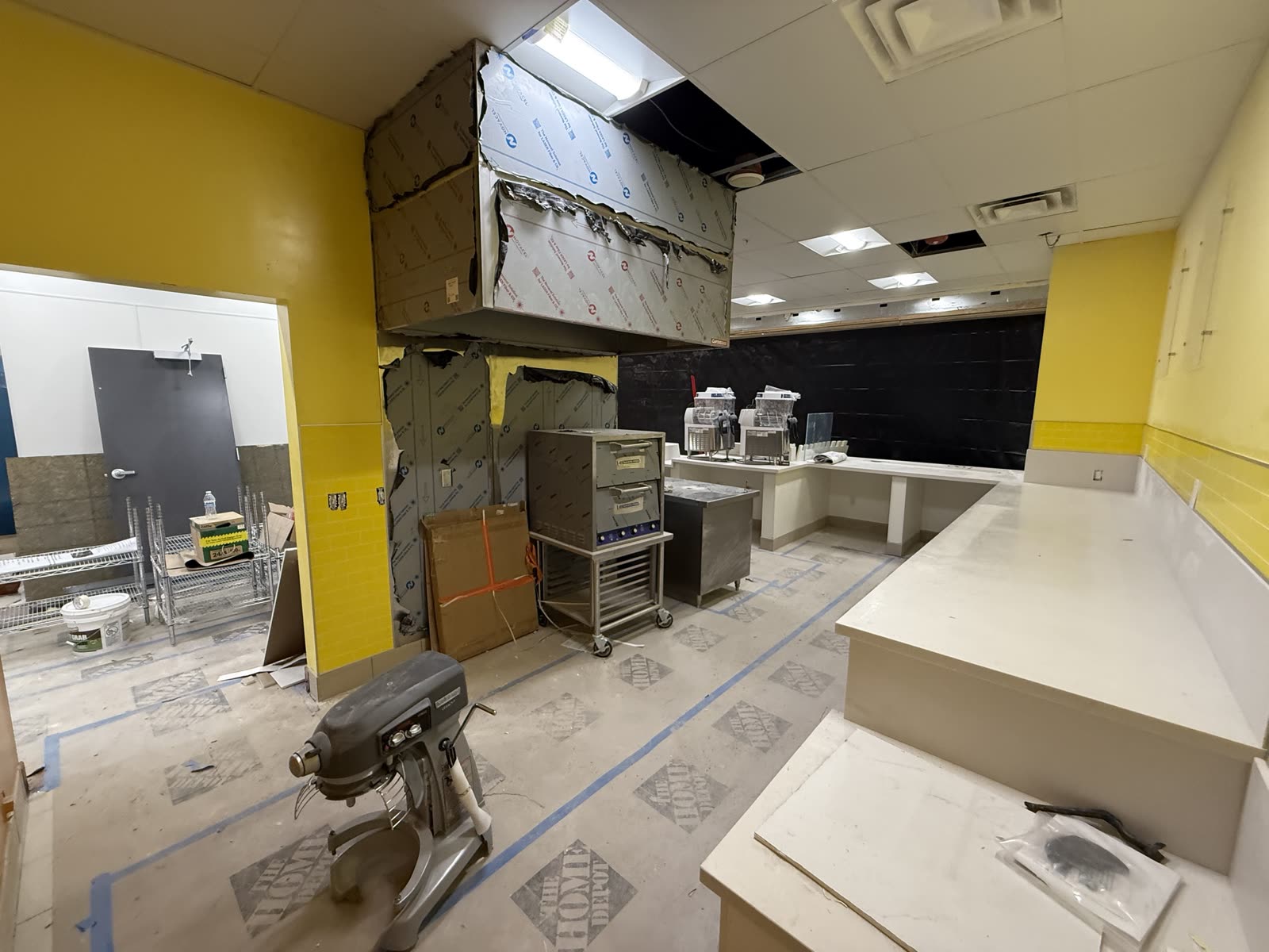 New exhaust hood boxed out and hung over the bake line with yellow tile wainscot and the counter run behind it